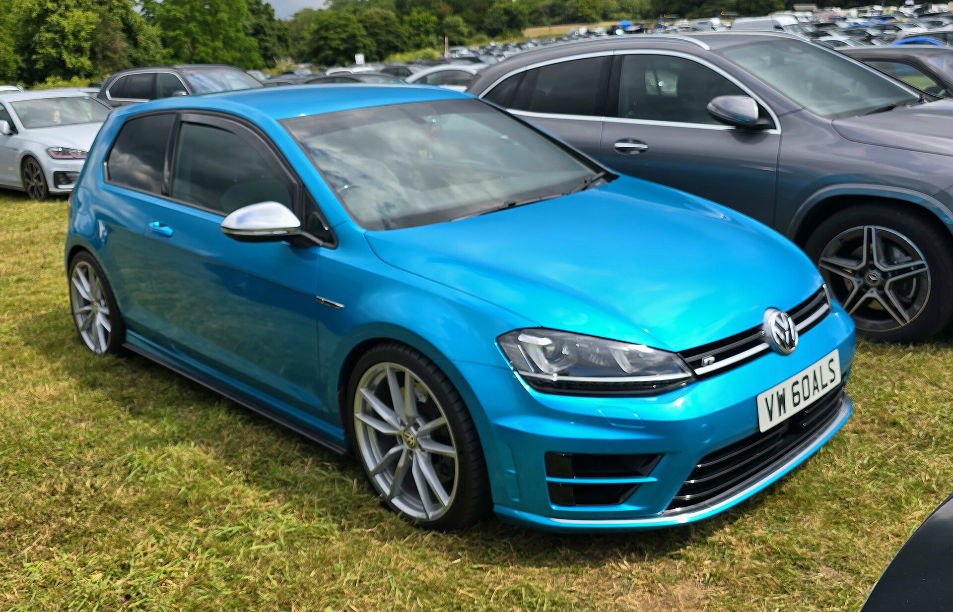 Blue Volkswagen Golf R parked on grass at an automotive event.