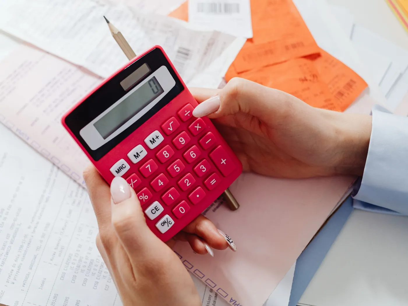 Hands holding a red calculator over printed household budget papers.