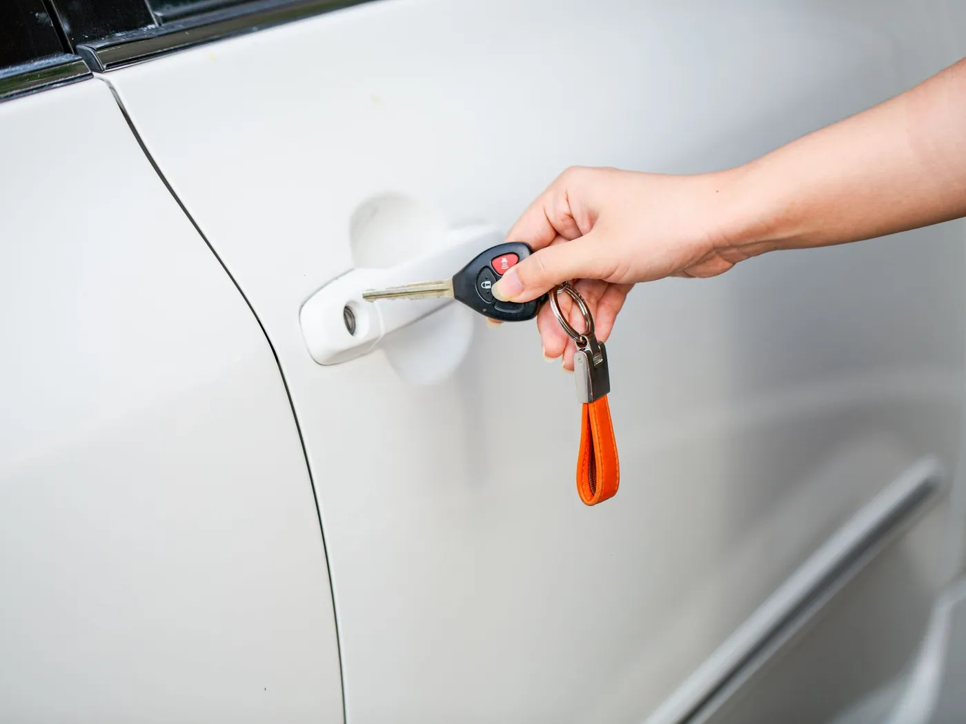 Hand holding a car key fob next to the door handle of a white car.