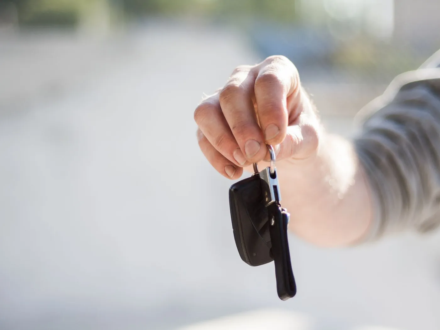 Hand holding out a car key, ready to hand it over.