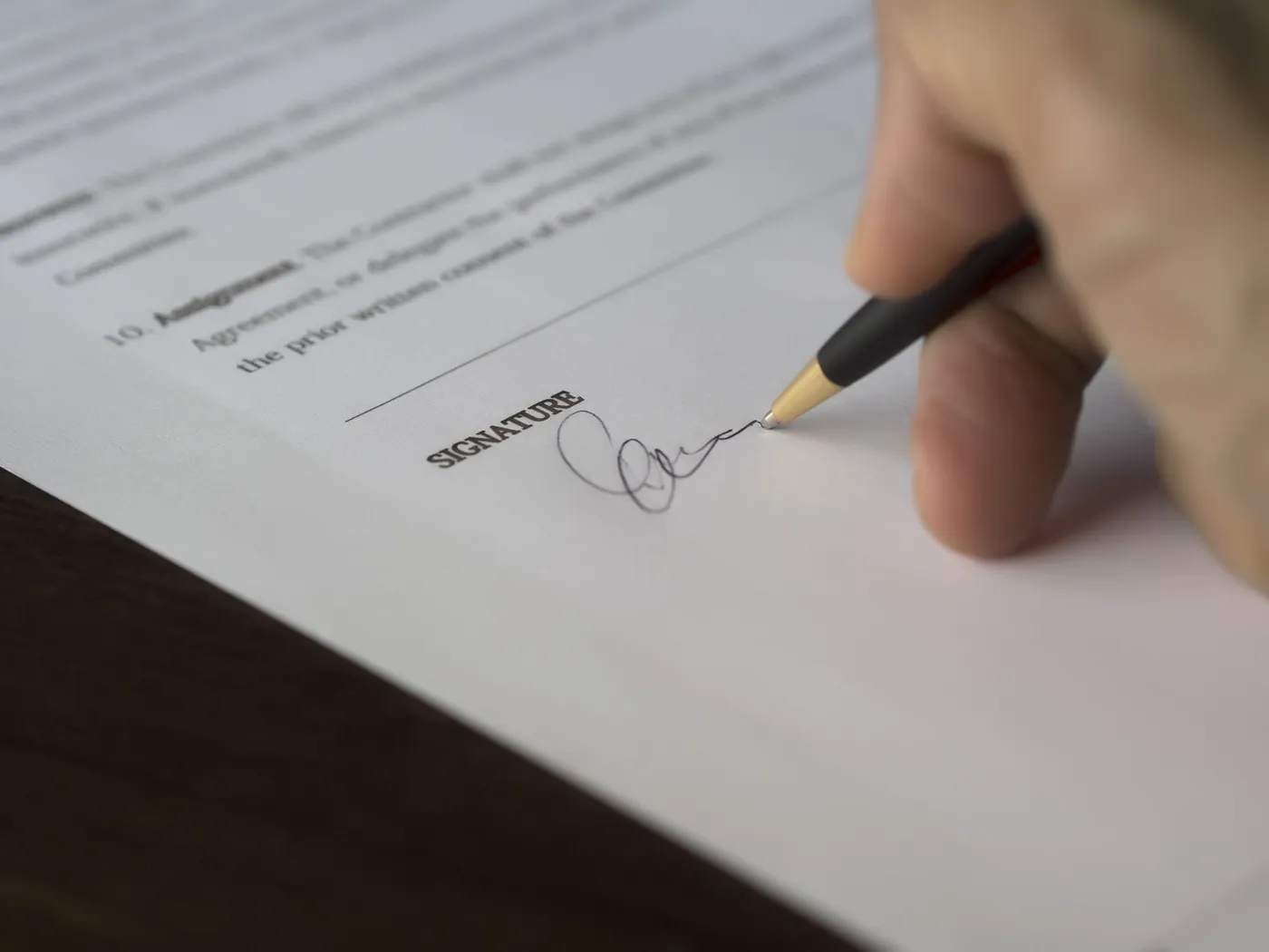 Close-up of a hand signing a printed contract with a pen.
