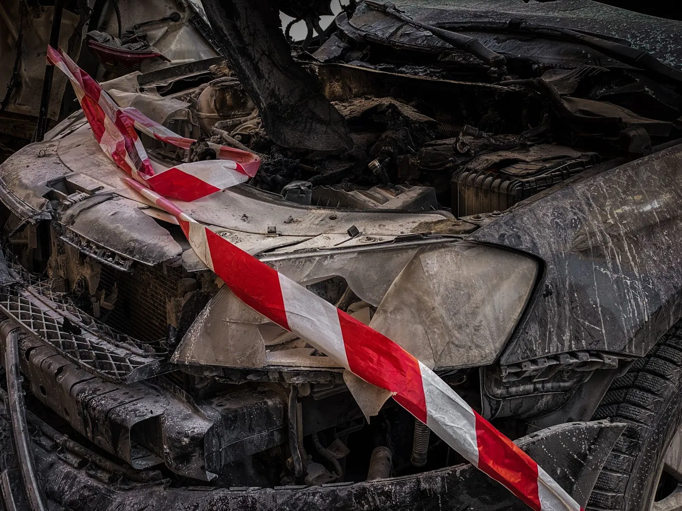 Close-up of a car's crushed front end wrapped in red-and-white barrier tape.