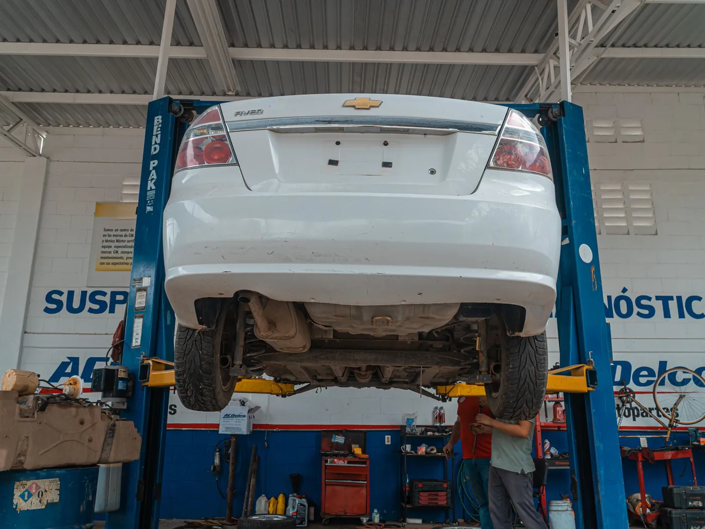 White car raised on a lift inside an auto repair shop.