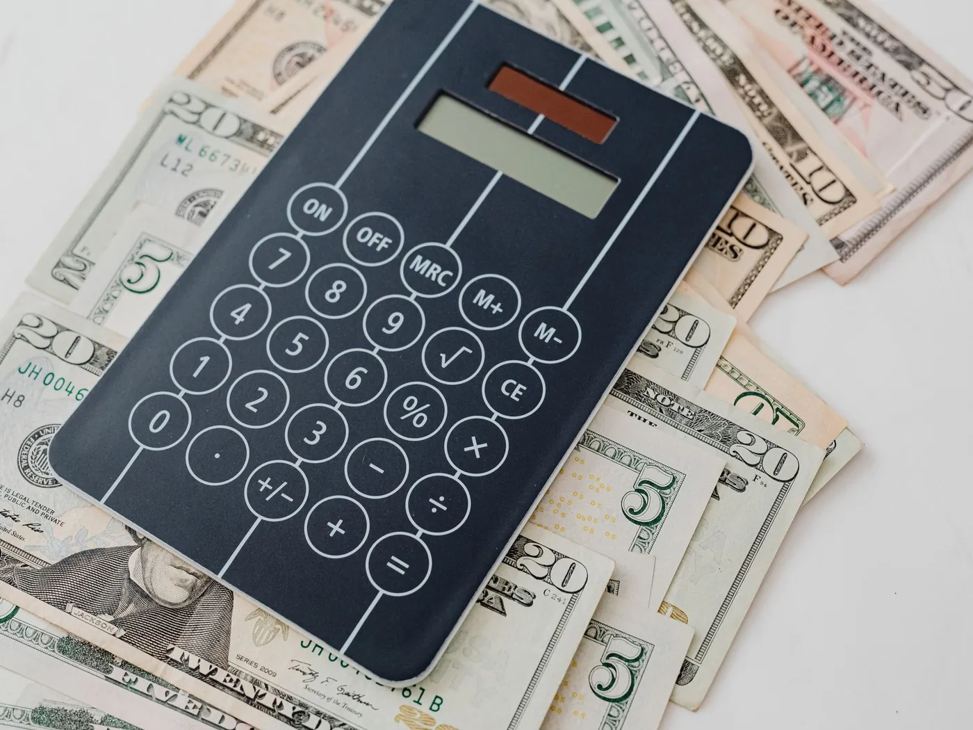 Black calculator resting on top of spread-out US dollar bills.