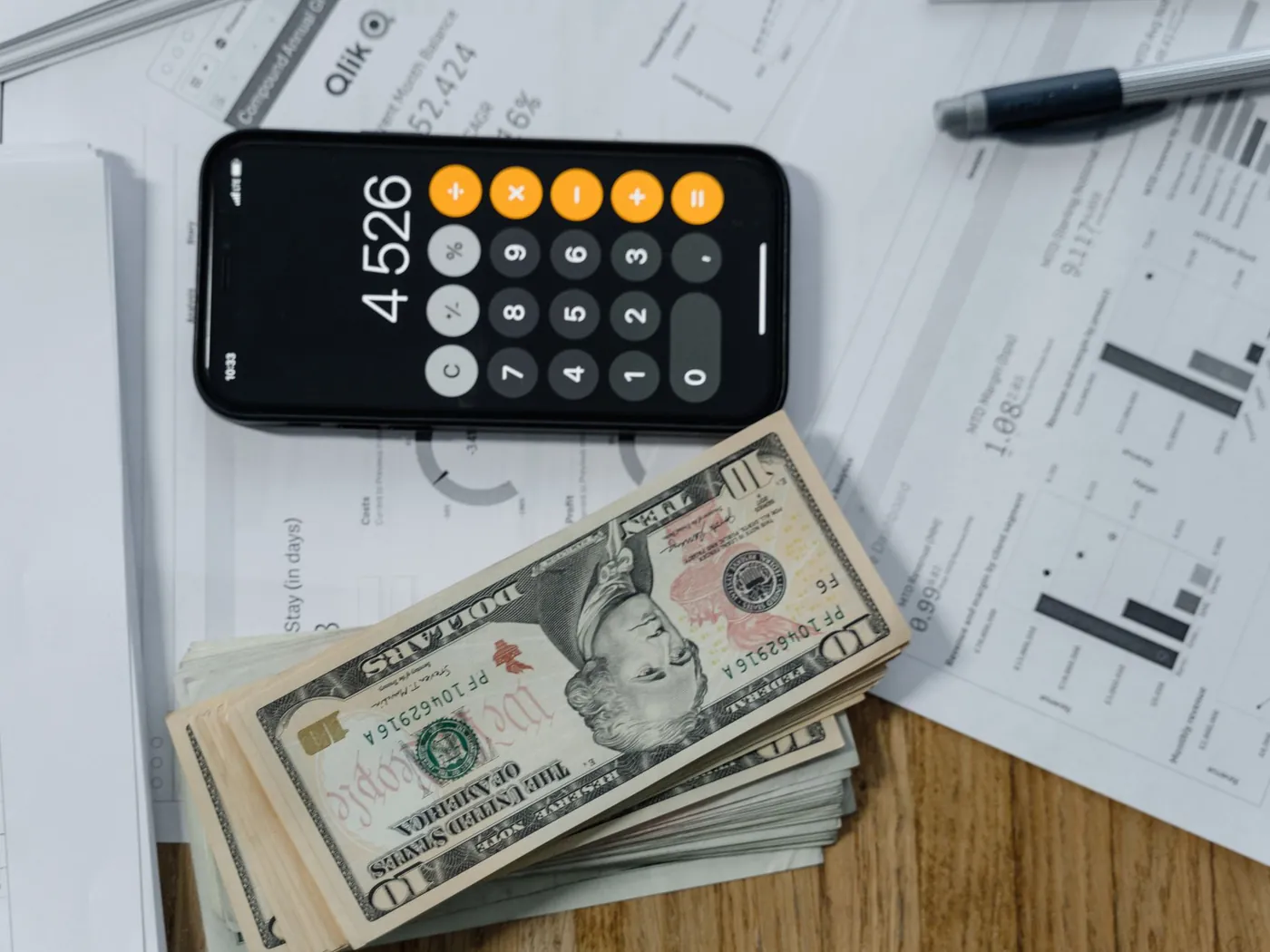 Calculator, dollar bills and printed paperwork spread on a desk.