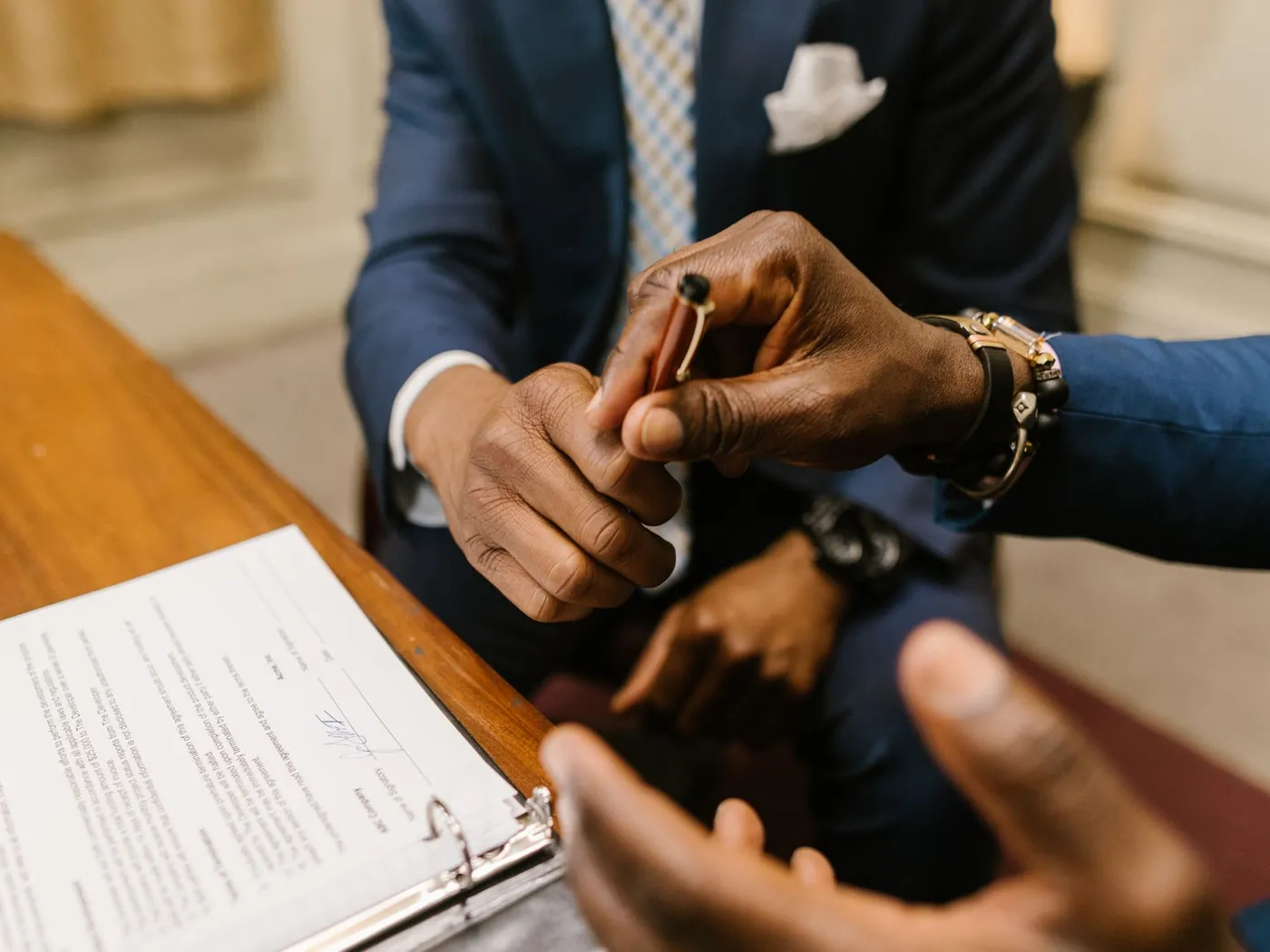 Two people at a desk, one handing a pen over a stack of purchase documents.