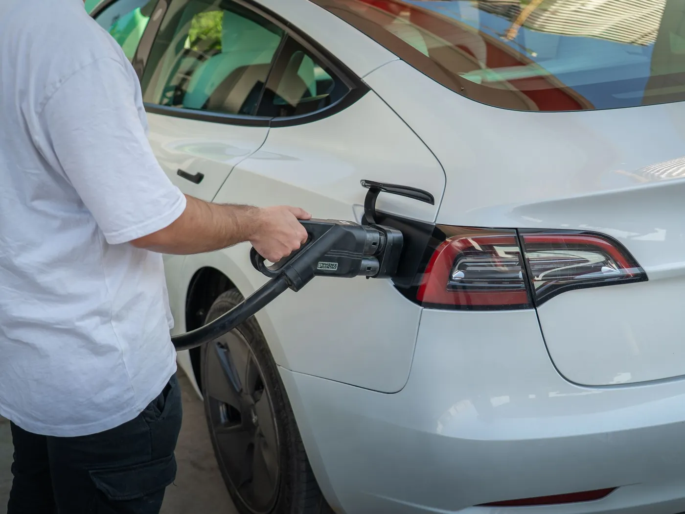 Person plugging a charging cable into a white electric car at a public charging station.
