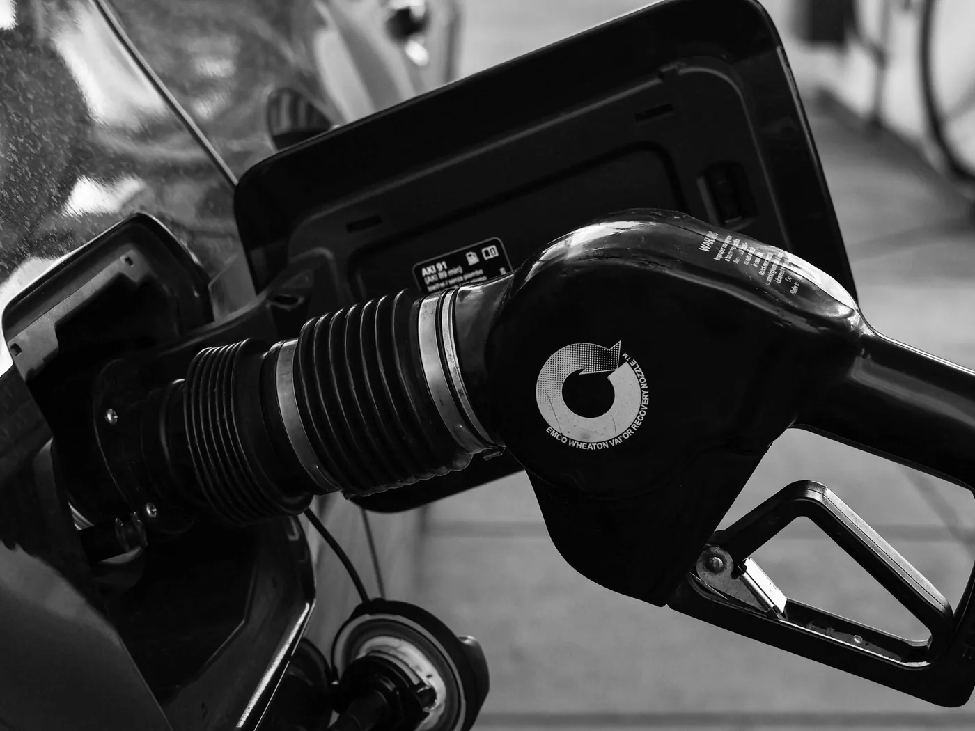 Black-and-white close-up of a fuel nozzle in a car's filler neck.