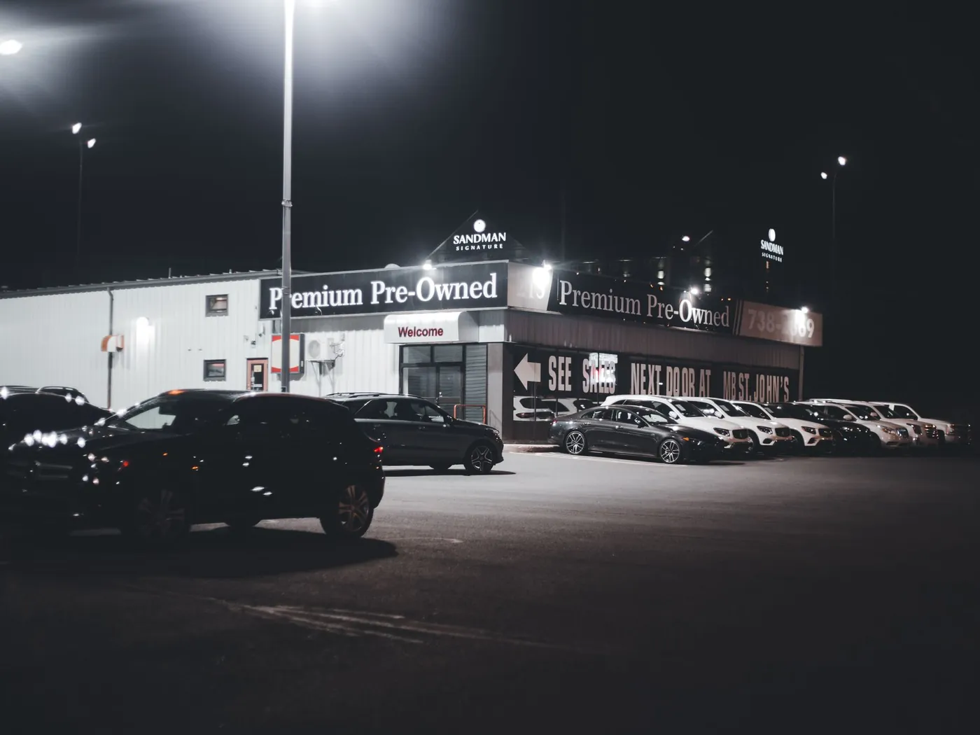 Pre-owned dealership lot at night with cars lined up under bright lights.
